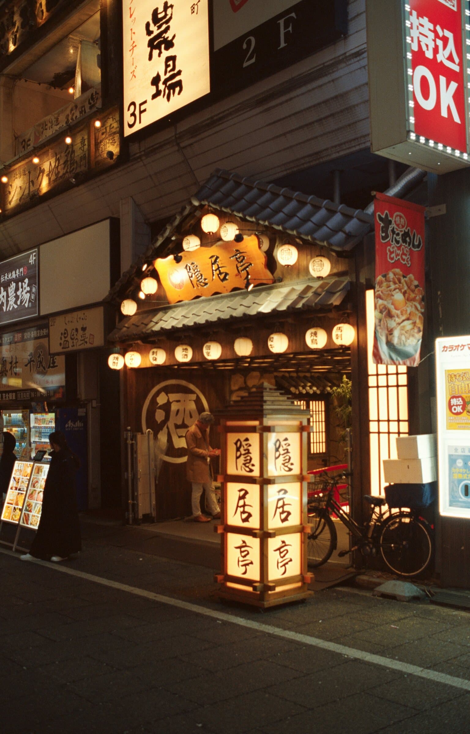 A Japanese izakaya entrance glowing with paper lanterns at night